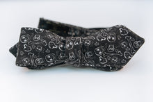  A black cotton bow tie with white printed designs of skulls and bones on this bold and rebellious bow tie.  Height: 1.75” x Width:5"   Knot Size: .75”  (Approx.)  Dry Clean Only