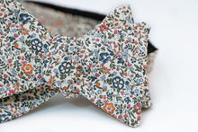 A lightweight cotton lawn bow tie hoast an array of spring forward hues like orange, light and dark blues and rosy red floral petals. This floral pattern is laying on a neutral beige solid background, perfect for any light and pastel shirts for the warmer weather to come.   Height: 3" x Width: 4.25" x Knot Size: .75  (Approx.)  Dry Clean Only