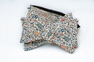 A lightweight cotton lawn bow tie hoast an array of spring forward hues like orange, light and dark blues and rosy red floral petals. This floral pattern is laying on a neutral beige solid background, perfect for any light and pastel shirts for the warmer weather to come.   Height: 3" x Width: 4.25" x Knot Size: .75  (Approx.)  Dry Clean Only