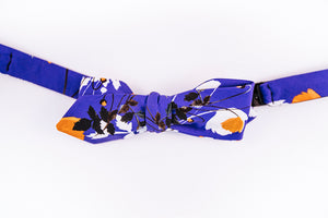 Liberty Of London Cotton Bow Tie With A Poppy Floral Design. A Orange Poppy dances on a solid blue background and abstract black and white floral patterns to tone down this bold slim diamond tip design. 