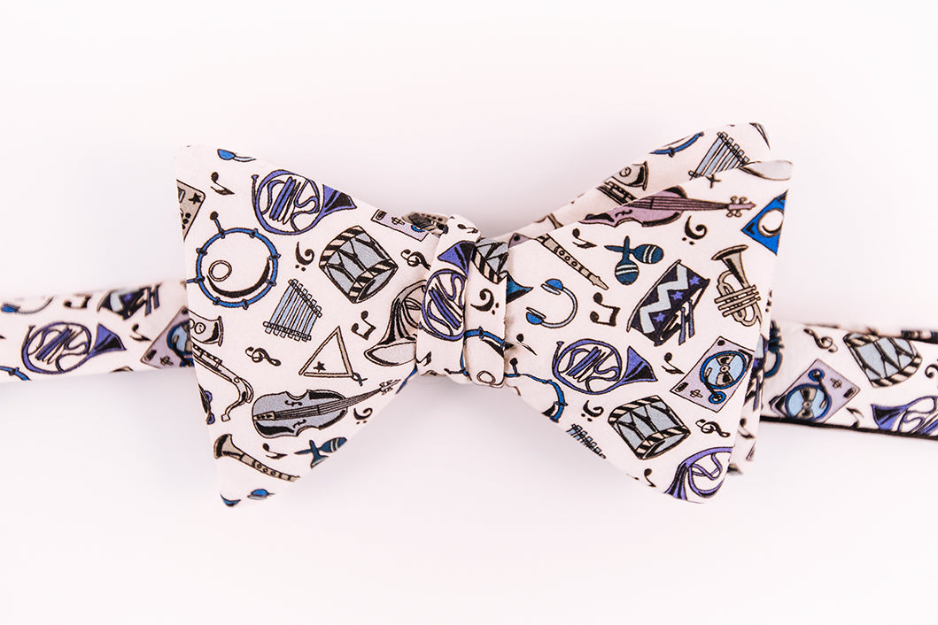 A array of musical instruments dancing on a solid beige background. Hosting instruments from violins, to snare drums, maracas, and many other brass instruments on this cotton butterfly bow tie.