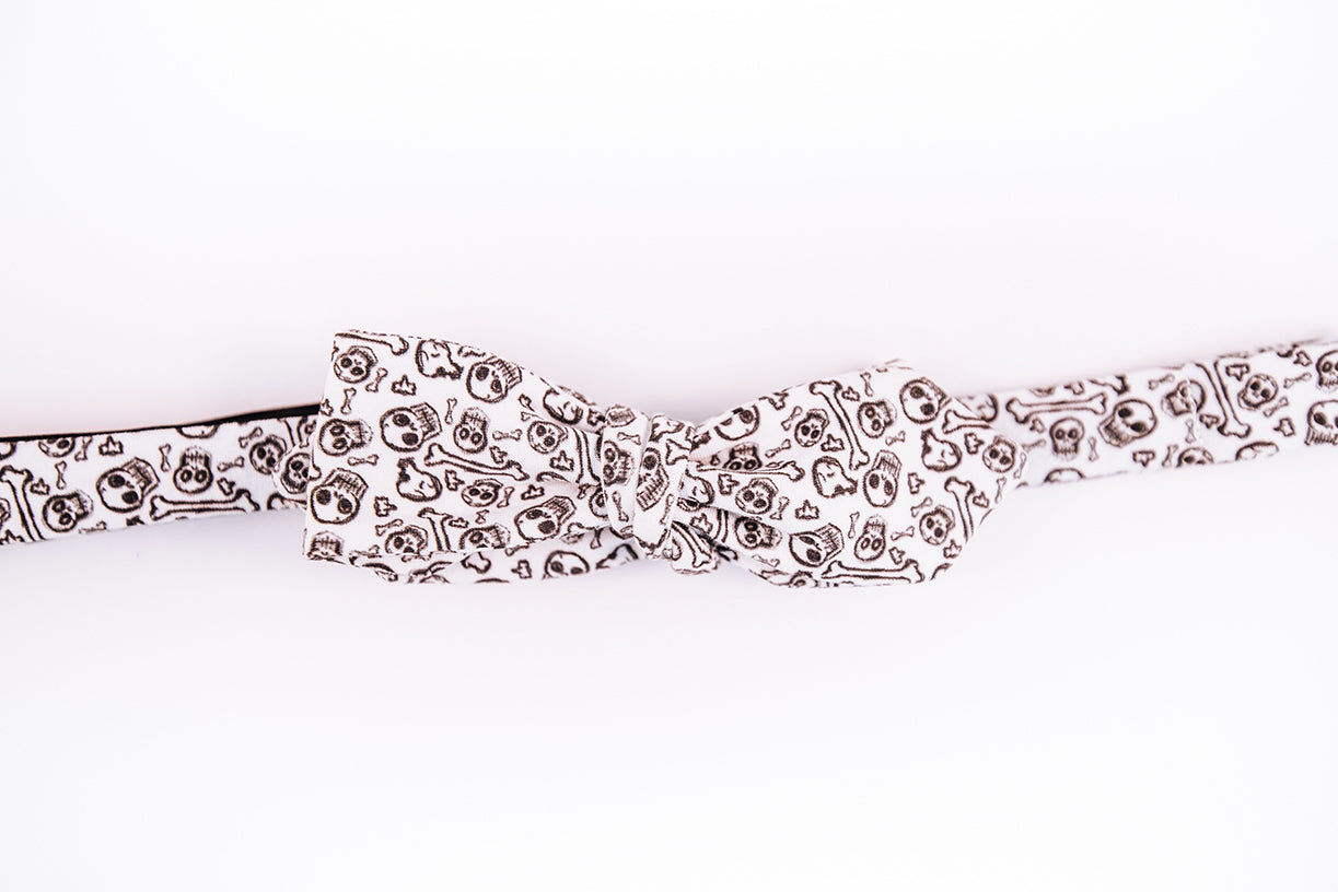 black skulls and bones pattern on this white cotton bow tie with a slim diamond tip design.